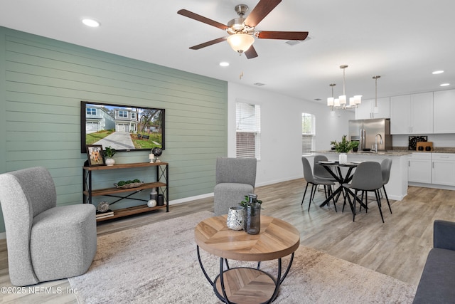 living room with recessed lighting, wooden walls, baseboards, light wood-style floors, and ceiling fan with notable chandelier