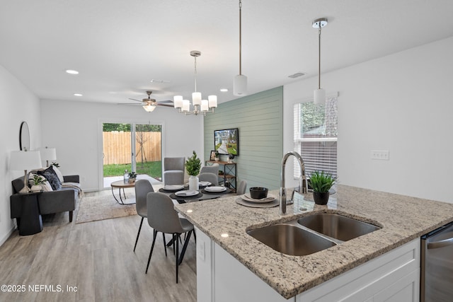 kitchen with a sink, white cabinets, open floor plan, light wood-type flooring, and decorative light fixtures