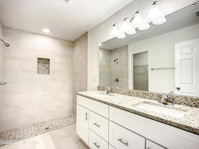 bathroom featuring a sink, a spacious closet, double vanity, and a tile shower