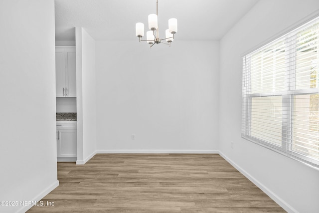 unfurnished dining area featuring an inviting chandelier, baseboards, and light wood finished floors