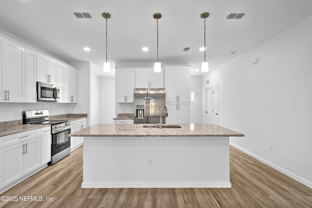 kitchen featuring a center island with sink, light wood-type flooring, appliances with stainless steel finishes, white cabinetry, and a sink