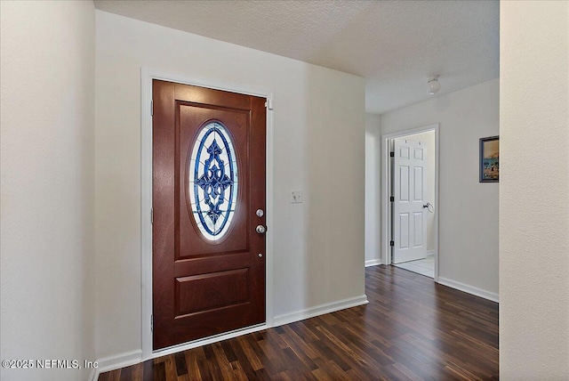 foyer entrance featuring a textured ceiling, dark wood-type flooring, and baseboards