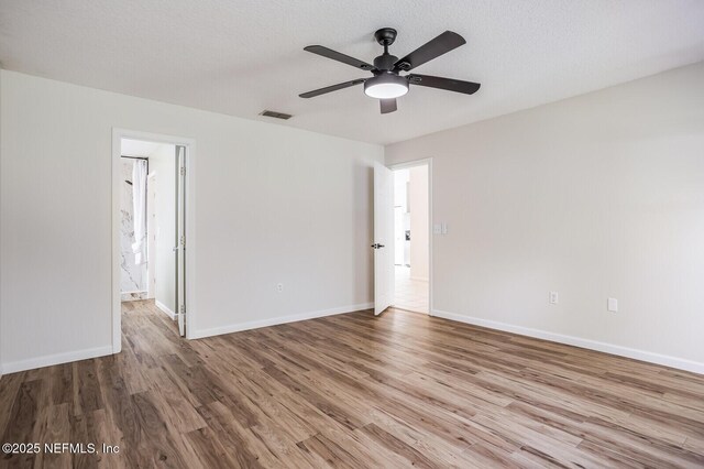 spare room with a ceiling fan, wood finished floors, visible vents, and baseboards