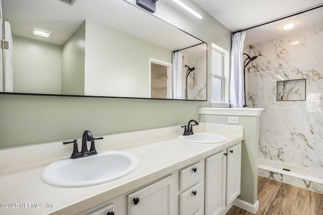 bathroom featuring double vanity, wood finished floors, a sink, and a marble finish shower