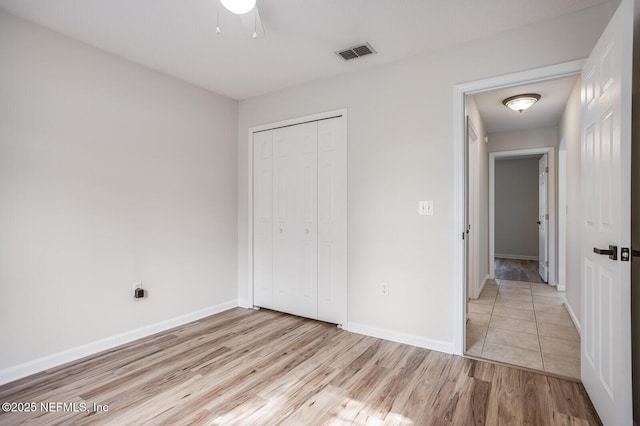 unfurnished bedroom with light wood finished floors, baseboards, visible vents, a ceiling fan, and a closet