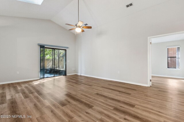 unfurnished room featuring a skylight, visible vents, wood finished floors, high vaulted ceiling, and baseboards