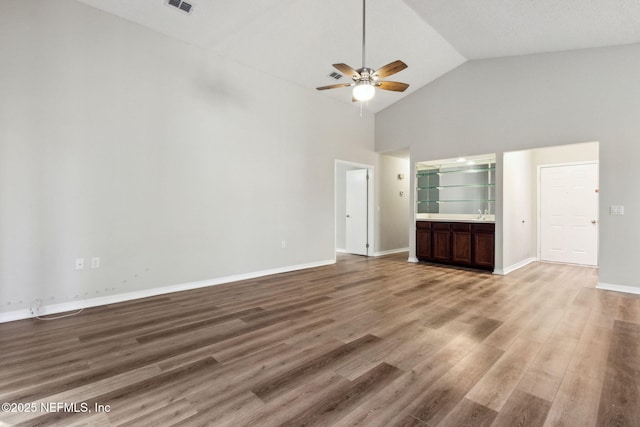 unfurnished living room featuring visible vents, baseboards, ceiling fan, wood finished floors, and high vaulted ceiling