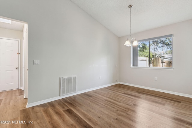 unfurnished room with a notable chandelier, wood finished floors, visible vents, baseboards, and vaulted ceiling