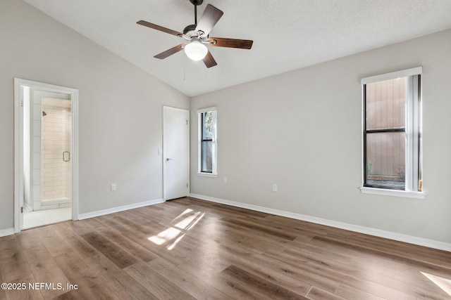 unfurnished bedroom with baseboards, a ceiling fan, lofted ceiling, ensuite bath, and wood finished floors