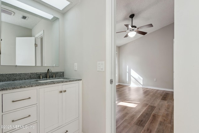 bathroom with a textured ceiling, vaulted ceiling with skylight, wood finished floors, and visible vents