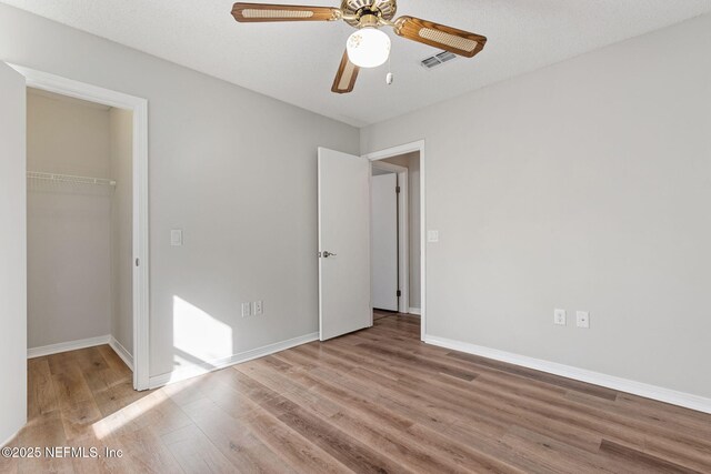 unfurnished bedroom with a walk in closet, a closet, visible vents, wood finished floors, and baseboards