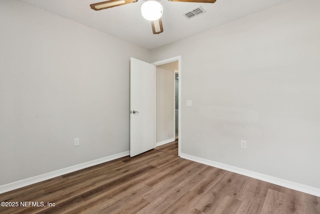 unfurnished room with ceiling fan, a textured ceiling, wood finished floors, visible vents, and baseboards