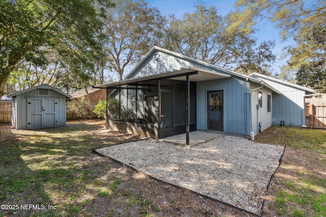 back of house with an outbuilding, fence, a sunroom, a storage unit, and a patio area