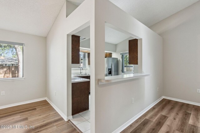 kitchen with a textured ceiling, light countertops, light wood-style floors, and stainless steel fridge with ice dispenser