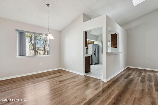 interior space featuring baseboards, lofted ceiling with skylight, wood finished floors, and an inviting chandelier