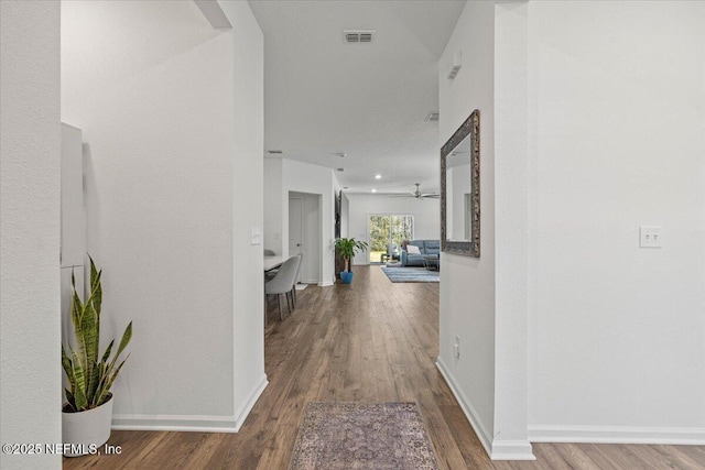 hall with wood finished floors, visible vents, and baseboards