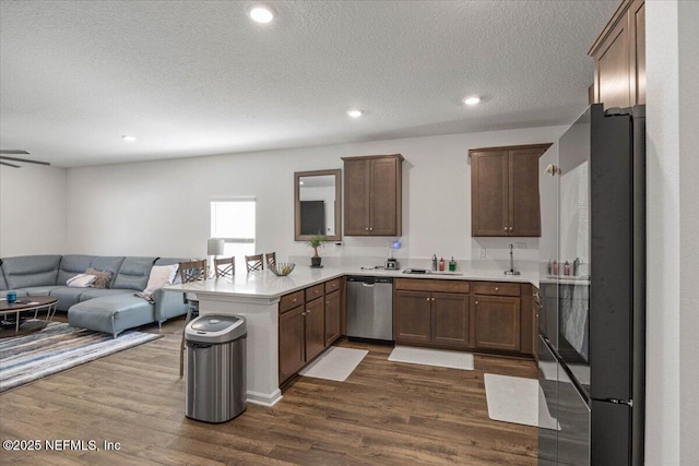 kitchen featuring a peninsula, a sink, dark wood-style floors, open floor plan, and dishwasher