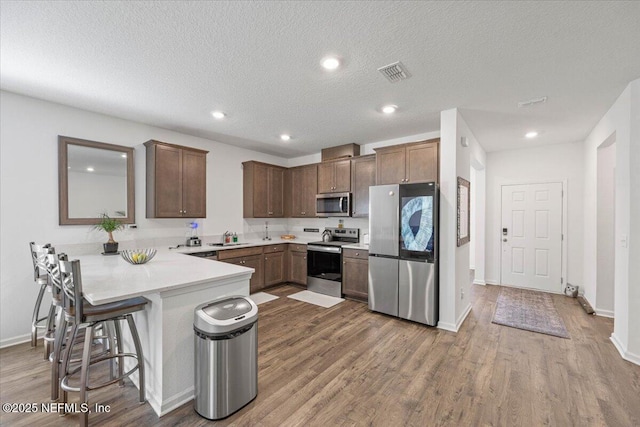 kitchen with a peninsula, wood finished floors, a sink, visible vents, and appliances with stainless steel finishes