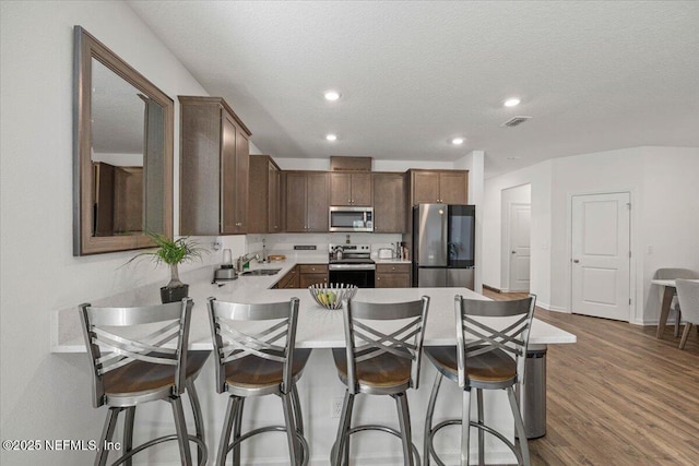 kitchen featuring a kitchen breakfast bar, dark wood-type flooring, stainless steel appliances, light countertops, and a sink