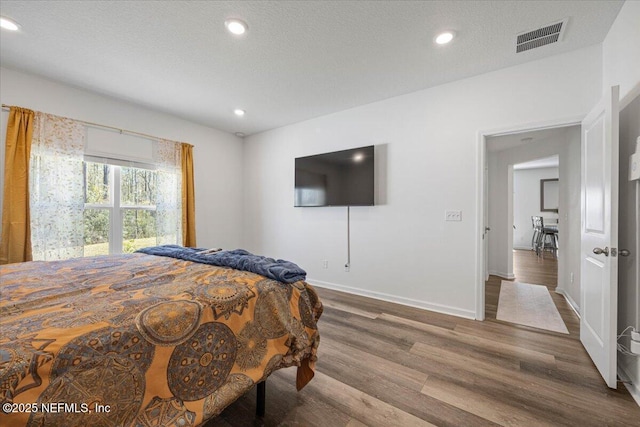 bedroom featuring baseboards, visible vents, wood finished floors, a textured ceiling, and recessed lighting