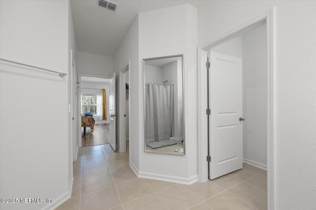 hall featuring baseboards, visible vents, a textured ceiling, and light tile patterned flooring