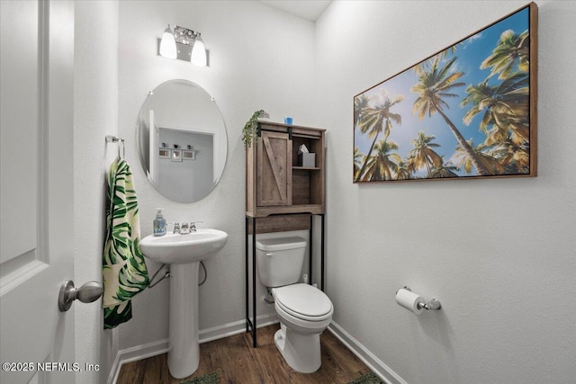 half bath with baseboards, a sink, toilet, and wood finished floors