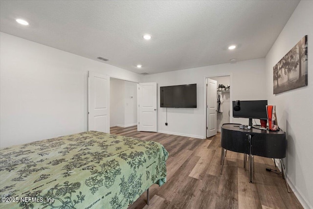 bedroom featuring a textured ceiling, wood finished floors, visible vents, baseboards, and a spacious closet