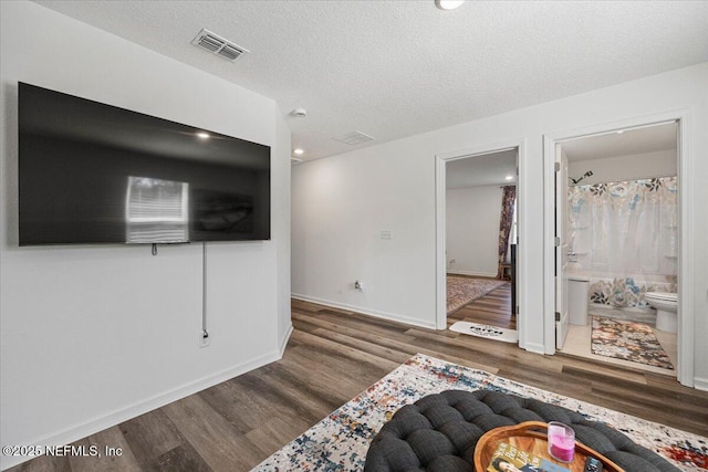 interior space featuring a textured ceiling, wood finished floors, visible vents, and baseboards