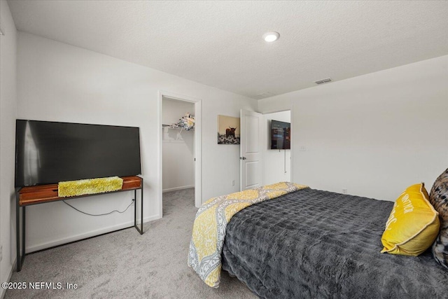 carpeted bedroom with a closet, visible vents, a walk in closet, and a textured ceiling