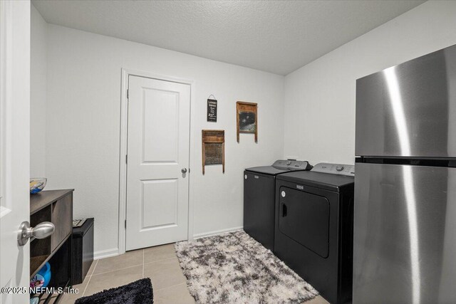 clothes washing area with light tile patterned floors, a textured ceiling, washing machine and dryer, laundry area, and baseboards