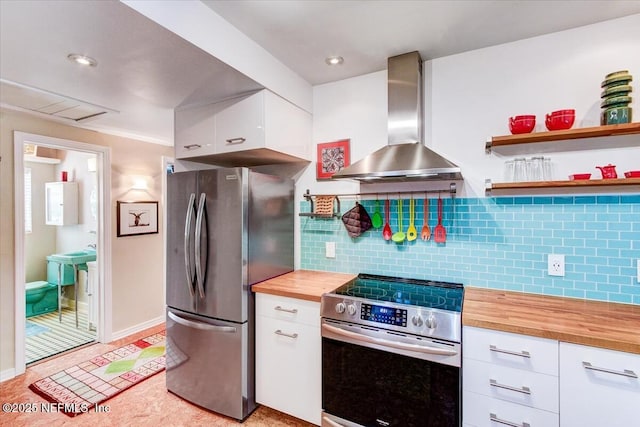 kitchen with tasteful backsplash, appliances with stainless steel finishes, white cabinets, wall chimney range hood, and butcher block countertops