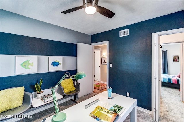 carpeted office featuring baseboards, visible vents, a ceiling fan, and a textured wall