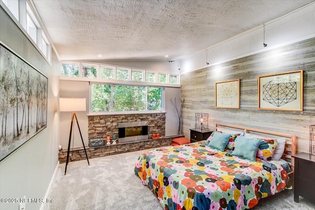 bedroom with a textured ceiling, a stone fireplace, baseboards, vaulted ceiling, and carpet