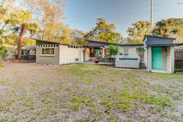 back of house featuring a patio, a jacuzzi, fence, a lawn, and stucco siding