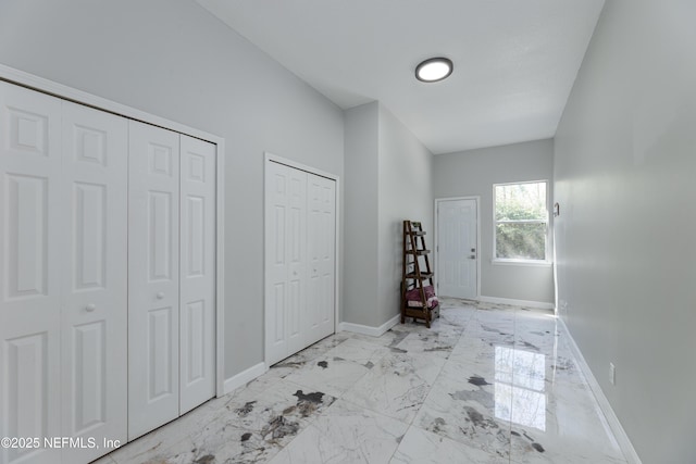 unfurnished bedroom featuring marble finish floor, baseboards, and two closets