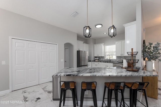 kitchen with arched walkways, marble finish floor, a breakfast bar area, stainless steel appliances, and a peninsula