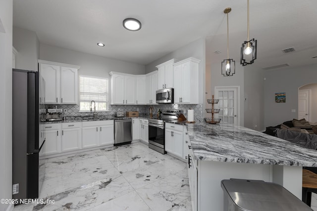 kitchen featuring arched walkways, marble finish floor, stainless steel appliances, a sink, and a peninsula