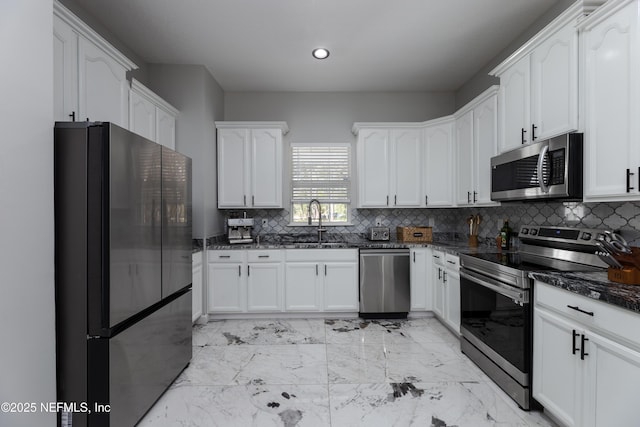 kitchen with stainless steel appliances, decorative backsplash, white cabinetry, a sink, and dark stone counters