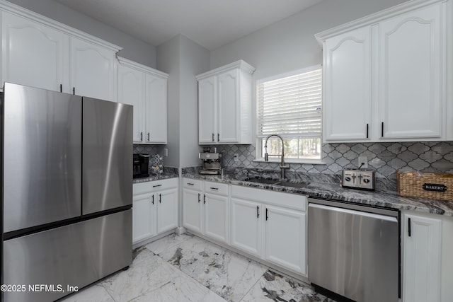 kitchen with white cabinets, appliances with stainless steel finishes, dark stone countertops, marble finish floor, and a sink