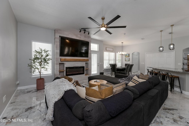 living area with marble finish floor, a fireplace, baseboards, and ceiling fan with notable chandelier