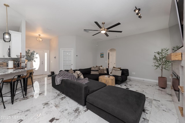 living area featuring arched walkways, marble finish floor, ceiling fan, and baseboards