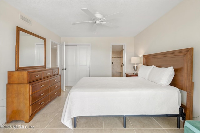 bedroom with visible vents, connected bathroom, light tile patterned floors, a closet, and a textured ceiling