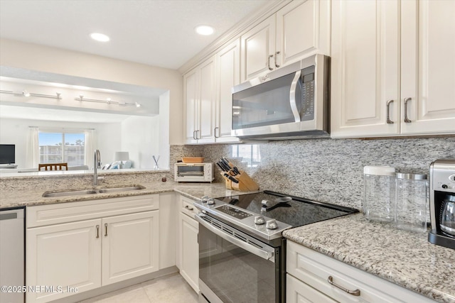 kitchen with light tile patterned floors, light stone countertops, a sink, appliances with stainless steel finishes, and tasteful backsplash