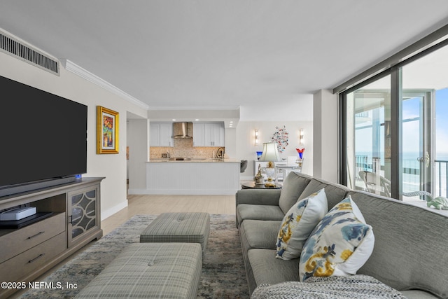 living area featuring baseboards, visible vents, ornamental molding, a wall of windows, and light wood-type flooring