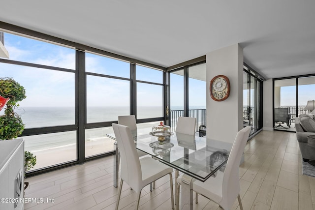 dining room with expansive windows, light wood finished floors, and a water view