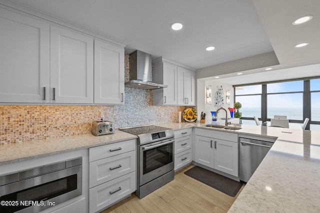 kitchen with stainless steel appliances, tasteful backsplash, white cabinetry, a sink, and wall chimney range hood