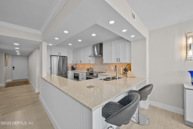 kitchen with stainless steel appliances, visible vents, a sink, wall chimney range hood, and light stone countertops