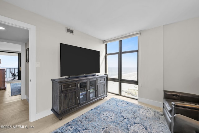 living room with expansive windows, light wood-type flooring, visible vents, and baseboards