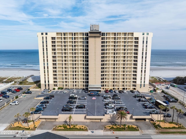 view of property with a water view, uncovered parking, and a view of the beach