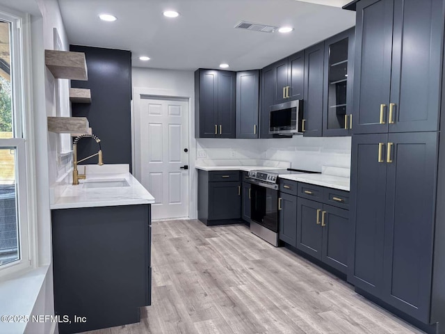 kitchen with visible vents, glass insert cabinets, light wood-type flooring, stainless steel appliances, and a sink